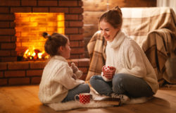 family mother and child drinking tea and laughing on winter evening by fireplace